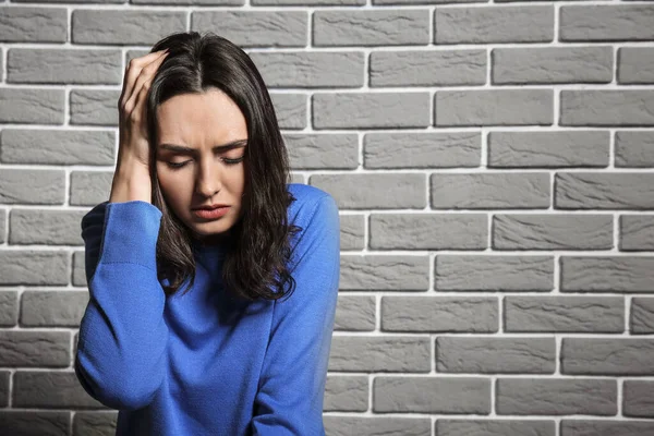 Depressed young woman near brick wall