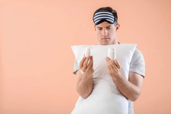 Young man with sleeping pills and pillow on color background