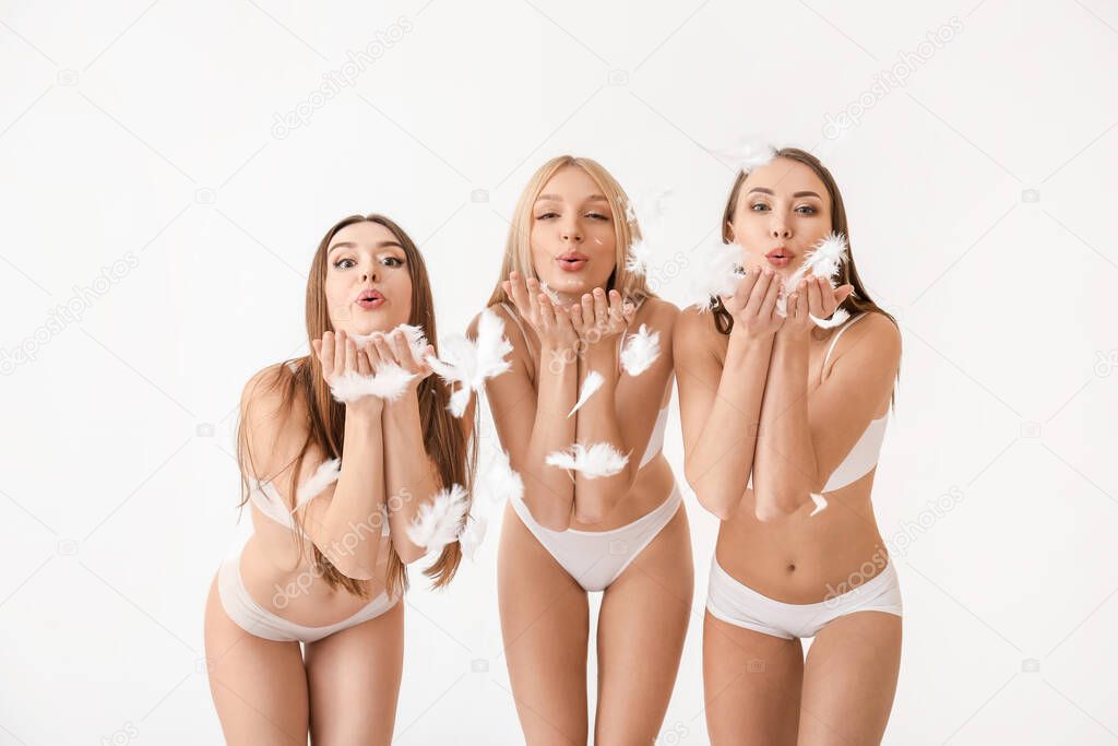 Beautiful young women in underwear playing with feathers on light background