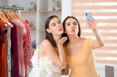 Genç kadınlar elbise mağazasında selfie çekiyorlar.