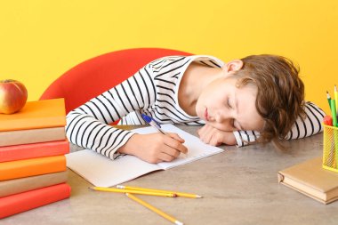 Ödev yapmak yerine masada uyuyan yorgun bir çocuk.