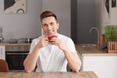 Yakışıklı adam mutfakta kahve içiyor.