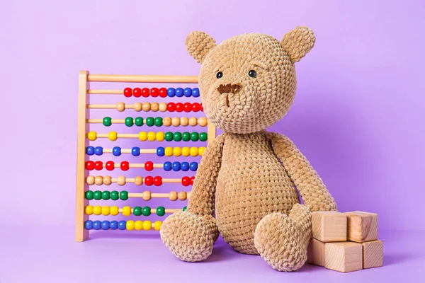 Teddy bear with abacus and cubes on color background