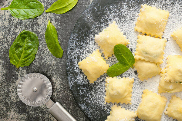 Raw ravioli with spinach and cutter on dark background