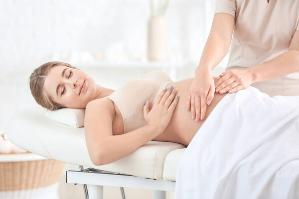 Молодая беременная женщина делает массаж в спа-салоне
