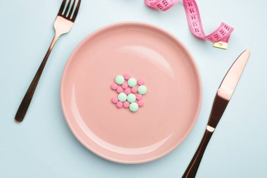 Kilo kaybı hapları, çatal bıçak takımı ve renkli arka planda mezura ile plaka