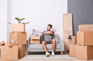 Evde yeni kıyafetleri olan genç bir adam var.