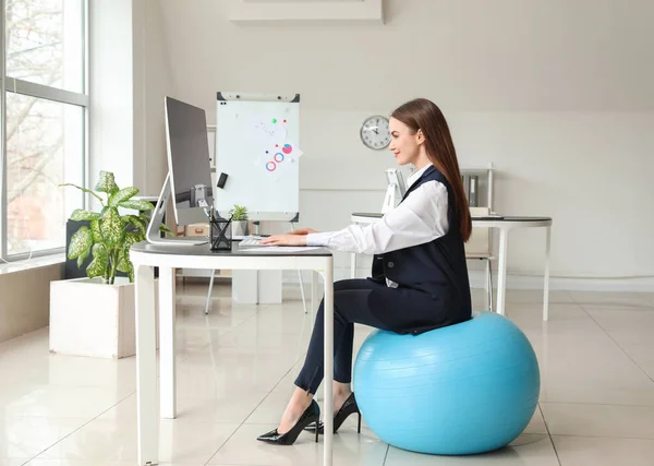 Businesswoman sitting on fitness ball while working in office