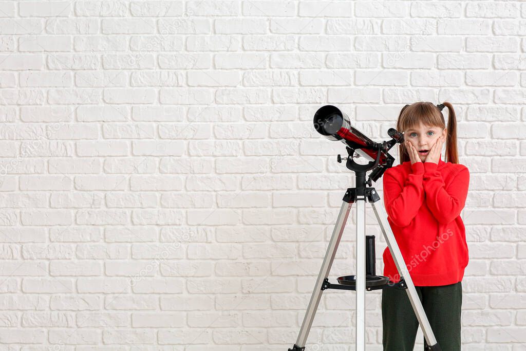 Cute surprised little girl with telescope on white brick background