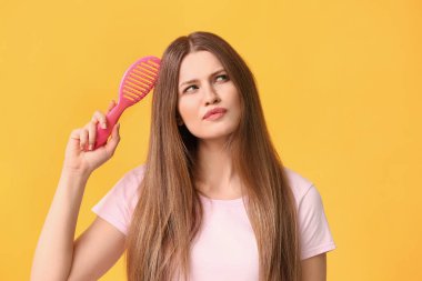 Renkli arka planda saç tarayan düşünceli genç bir kadın.