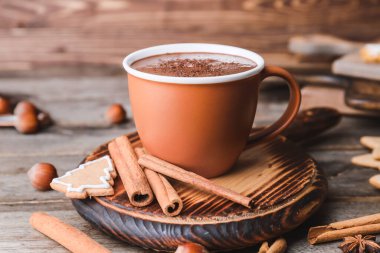 Bir fincan sıcak çikolata, tarçın ve ahşap arka planda kurabiyeler.