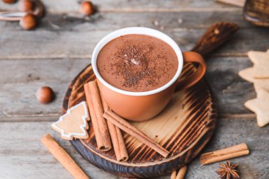 Bir fincan sıcak çikolata, tarçın ve ahşap arka planda kurabiyeler.