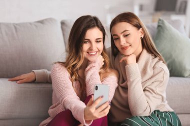 Sıcak kazaklı genç kadınlar evde selfie çekiyorlar.