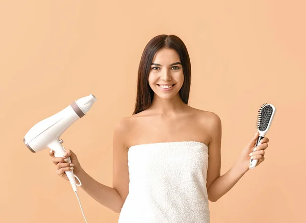 Beautiful young woman with hair dryer and brush on color background