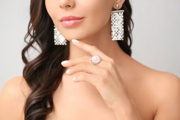 Young woman with beautiful jewelry on light background