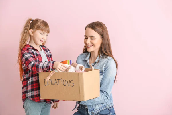 Volunteer with donations for orphans and little girl on color background