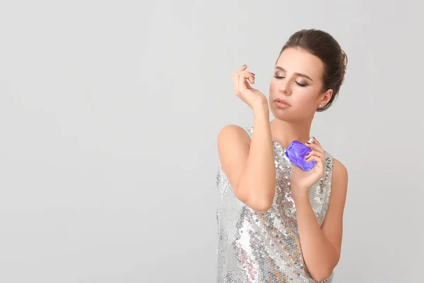 Beautiful young woman with perfume on grey background