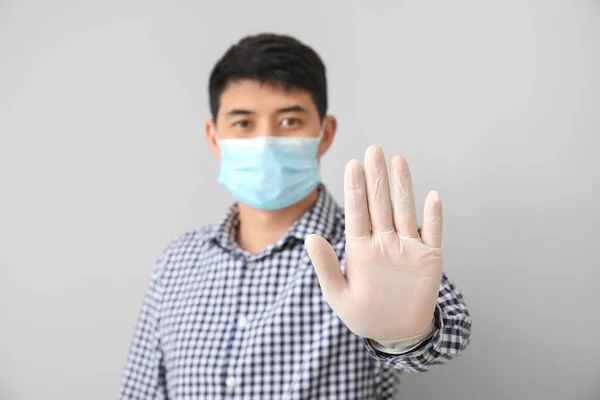Asian man in mask showing STOP gesture on light background. Concept of coronavirus epidemic