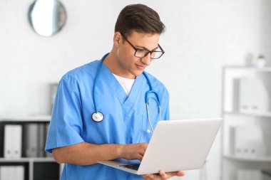 Klinikte dizüstü bilgisayarda çalışan erkek doktor.