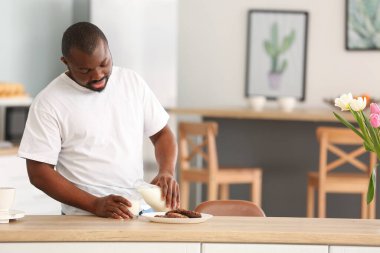 Afro-Amerikalı adam mutfakta süt içiyor.