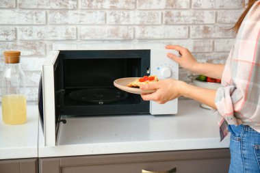 Woman putting plate with food in microwave oven clipart