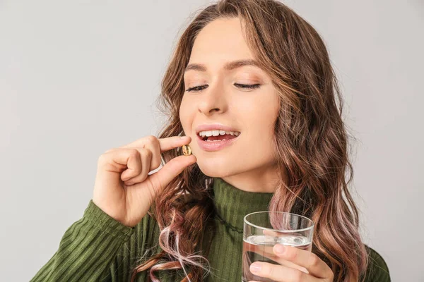 Young woman with fish oil on light background