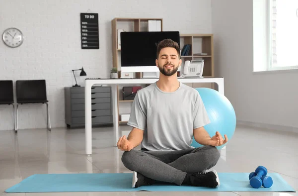 Sporty young man practicing yoga in office