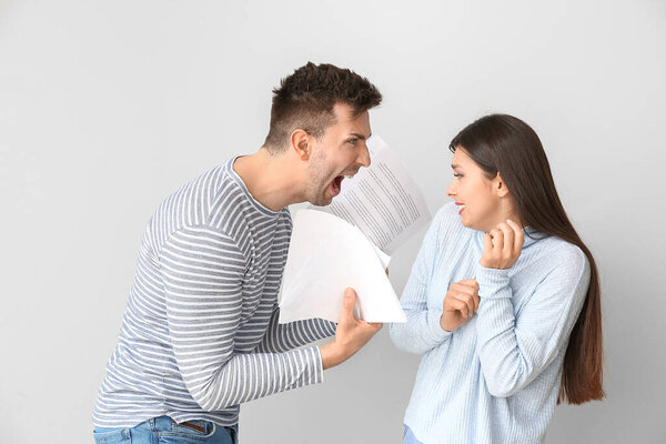 Displeased man scolding his wife for overspending on light background