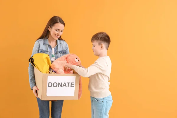 Volunteer with donations for orphans and little boy on color background