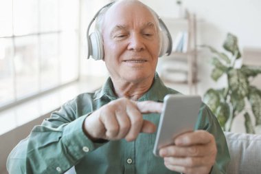 Evde cep telefonu ve kulaklığı olan yaşlı bir adam.
