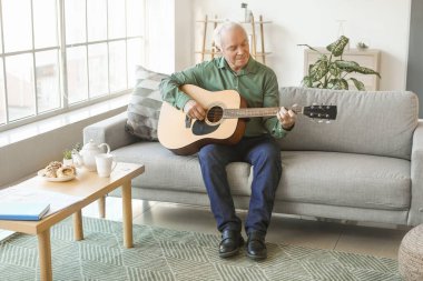 Evde gitar çalan yaşlı bir adam.