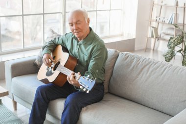 Evde gitar çalan yaşlı bir adam.