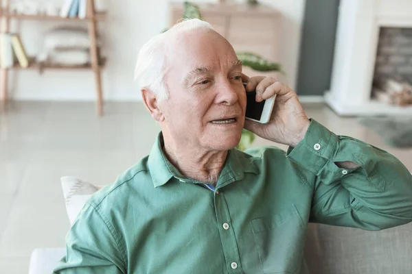 Elderly man talking by mobile phone at home