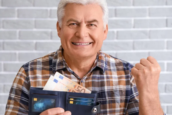 Happy senior man with purse on brick background