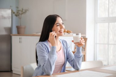 Mutfakta süt içerken telefonla konuşan güzel genç bir kadın.