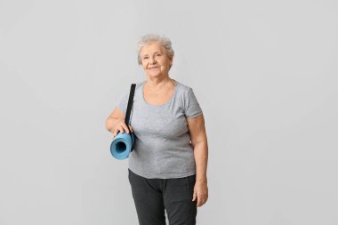 Hafif arka planda yoga minderi olan yaşlı bir kadın.