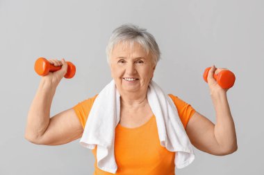 Hafif arka planda halterleri olan yaşlı kadın.