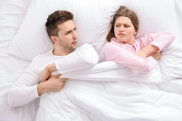 Young couple fighting for blanket in bed
