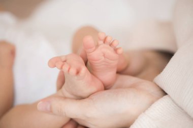 Annenin elleri küçük bebeğin minik ayaklarını tutuyor, yakın plan.