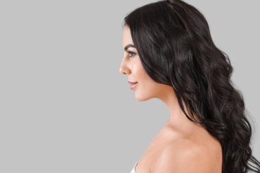 Gri arka planda güzel, sağlıklı saçları olan genç bir kadın.