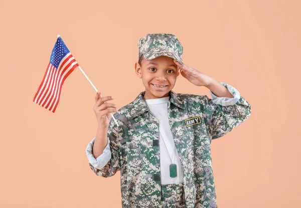 Little saluting African-American soldier with USA flag on color background