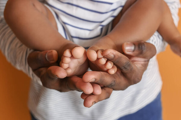 Happy African-American man with cute baby on color background, closeup