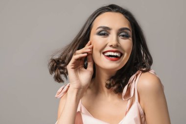 Gri arka planda güzel makyajlı genç bir kadın.