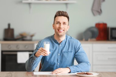 Genç adam mutfakta süt içiyor.