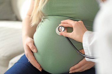 Klinikteki hamile kadını muayene eden doktor, yakın plan.