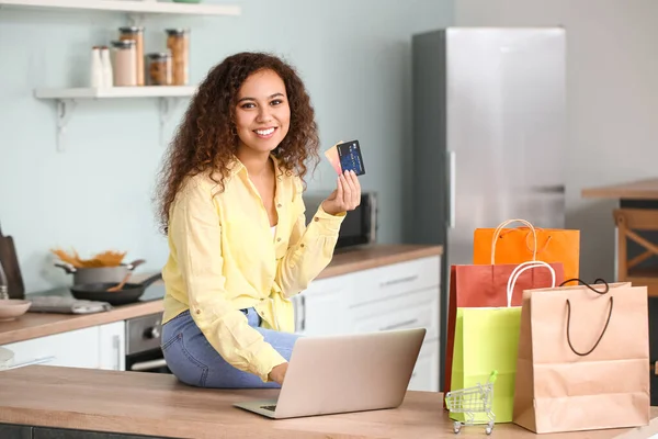 Young woman with laptop, credit cards and shopping bags at home