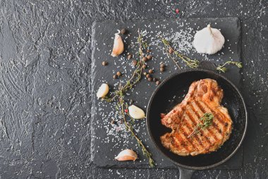 Kızarmış tavada pişmiş domuz bifteği ve koyu arkaplanda baharatlar.