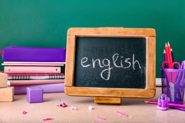 Sınıftaki masa üzerinde ENGLISH ve kırtasiye yazılı tebeşir tahtası