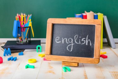 Sınıftaki masa üzerinde ENGLISH ve kırtasiye yazılı tebeşir tahtası