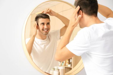 Evde saç tarayan yakışıklı genç adam.